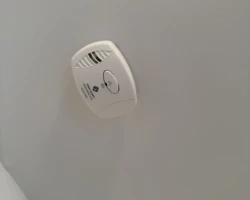 Carbon monoxide alarm mounted on a ceiling near a kitchen, with no smoke alarm present