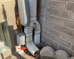 Downspout emptying onto the ground immediately beside a house foundation wall