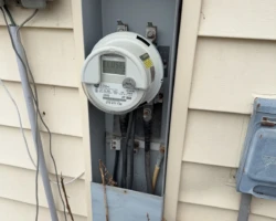 Exterior electric meter enclosure with the lower cover absent and wiring visible