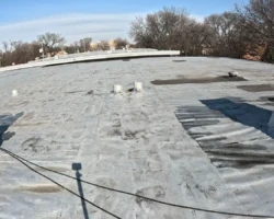 Flat roof membrane with numerous black asphalt cement patches and ponded areas