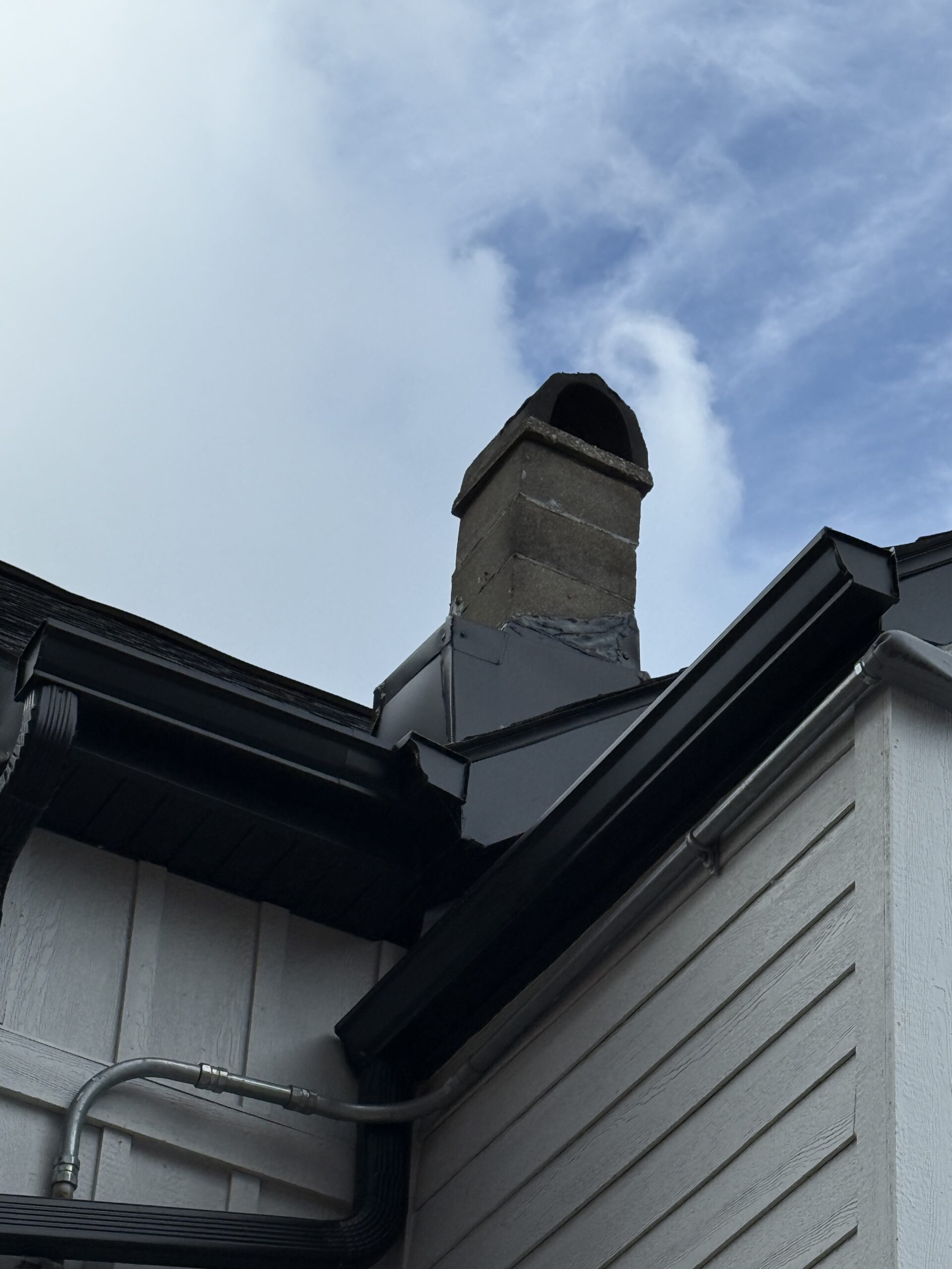 Chimney base sealed with black roofing tar instead of metal step flashing where it meets the shingles