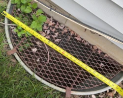 Cramped metal window well around a basement egress window, too small for safe escape